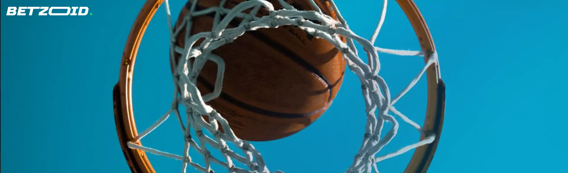 A basketball scoring a basket, viewed from below against a clear blue sky.