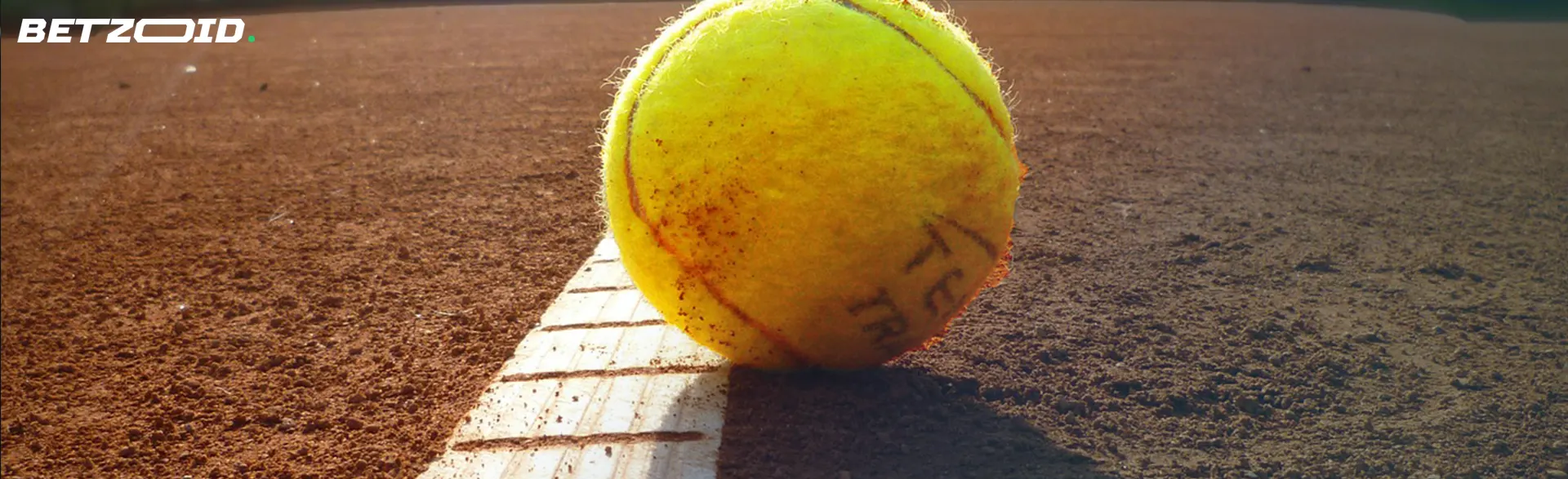 Close-up of tennis ball on a clay court, resting on the white boundary line.