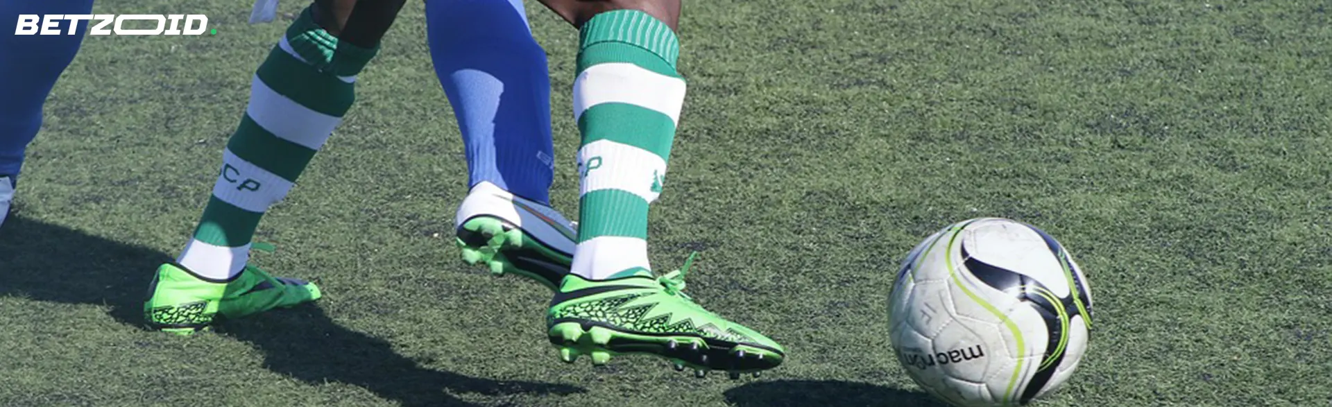 A close-up shot of a football player's feet in green and white striped socks and green shoes, ready to kick a football.