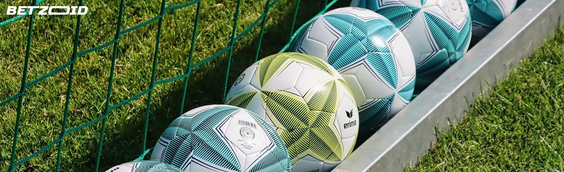 A vibrant display of variously designed footballs lined up behind the goal net on a grassy field.
