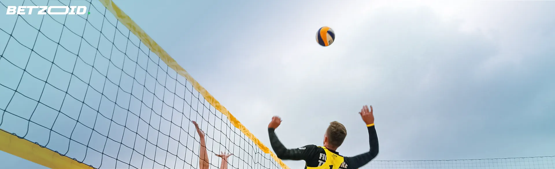 Game of volleyball is being played, the ball flies over the net after a player hits it.