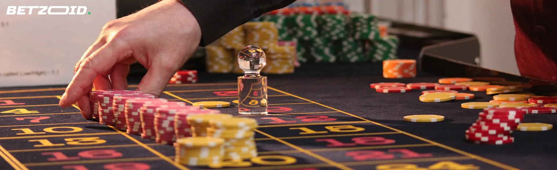 A dealer's hand moving chips on a blackjack table, with cards and chip stacks.