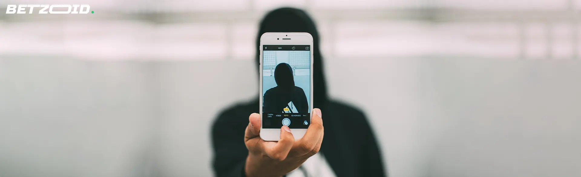 Person using a smartphone to photograph a mysterious figure in a hoodie, representing the discreet and secure features of anonymous sportsbooks in Canada.