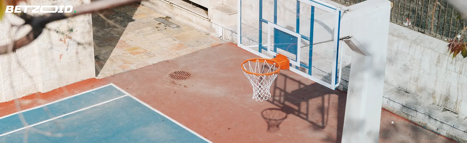 A sunlit outdoor basketball court featuring a hoop and net.