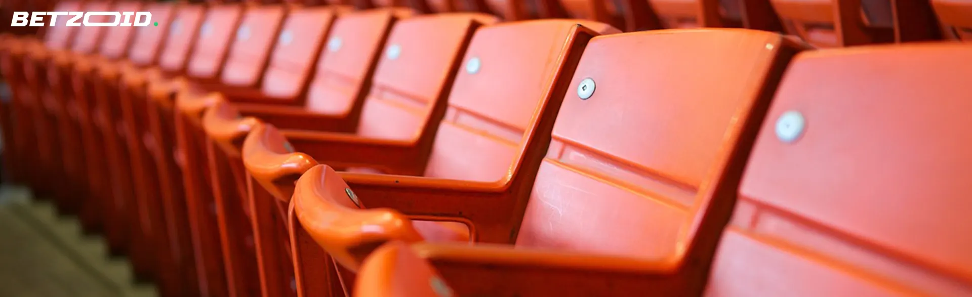 Long row of empty coral red stadium seats with a blurred background.
