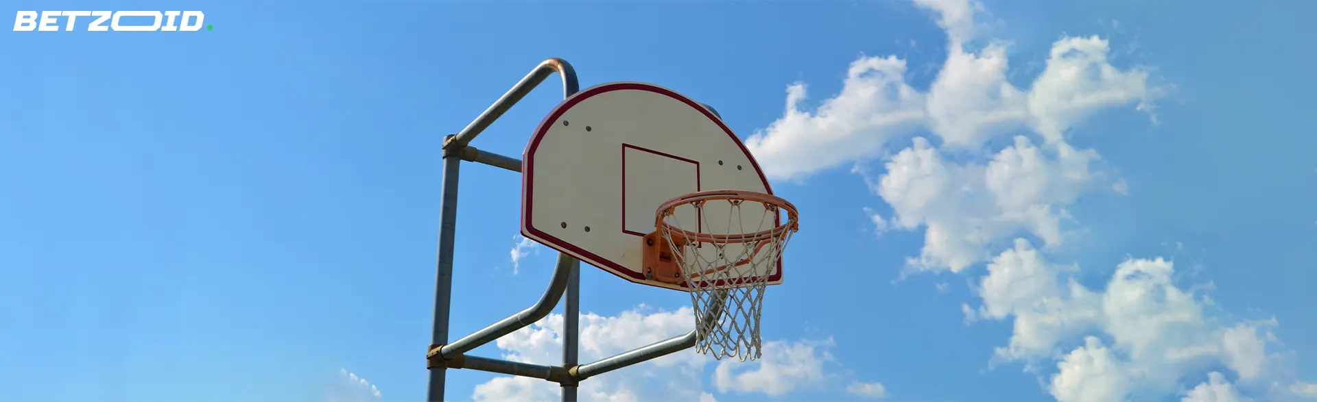 A basketball hoop set against a clear blue sky with scattered clouds, highlighting cash-out options at bookmakers in Canada.