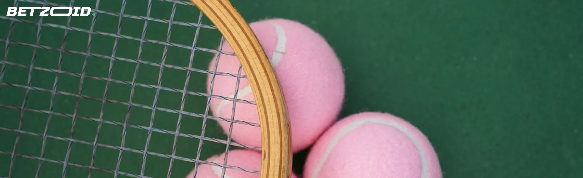 Three pink tennis balls positioned behind a tennis racket on a green court.