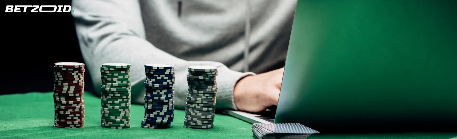 Un hombre usa una computadora portátil con montones de fichas de póquer a su lado para casinos dinero real gratis sin deposito.