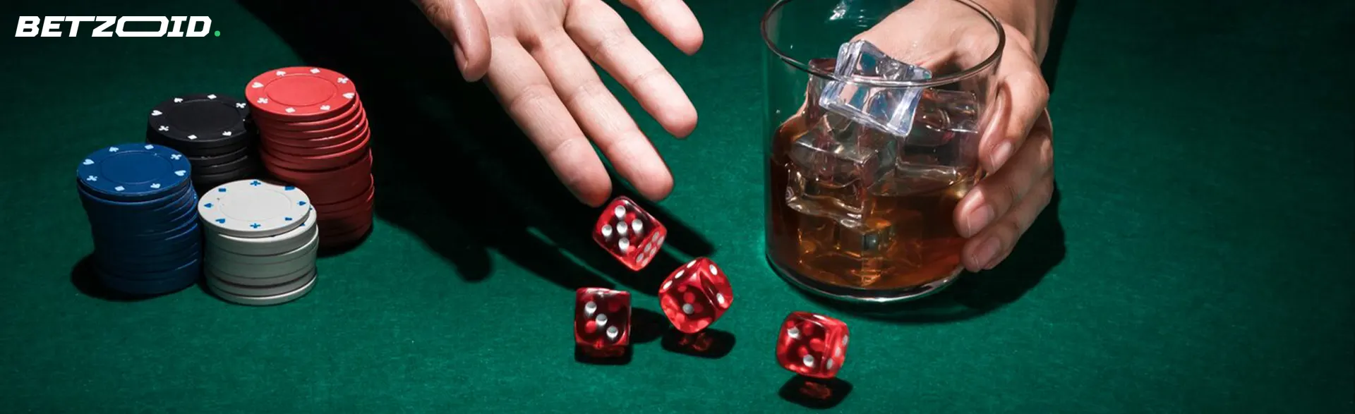 The player rolls the dice on the table next to the chips and the drink in the glass.