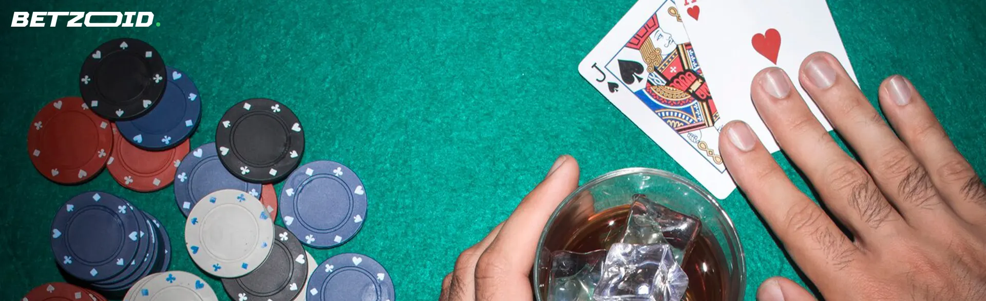Un joueur tient des cartes à côté des jetons de casino et une boisson dans un verre.