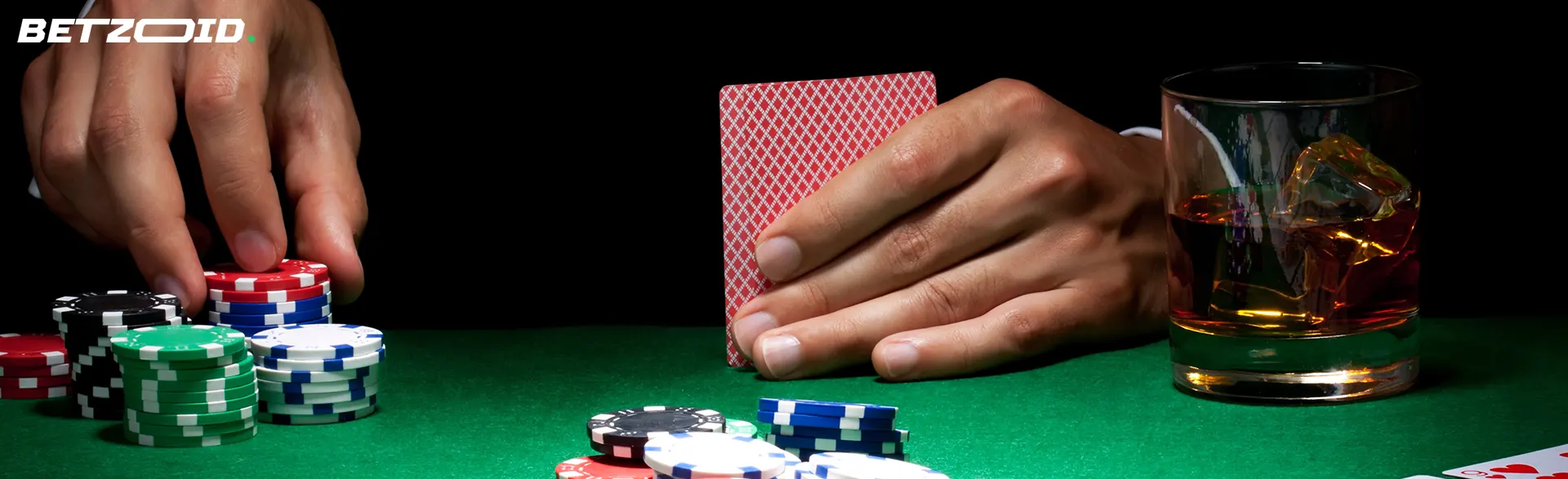 Cartes dans les mains du joueur à côté des jetons de casino et d'une boisson dans un verre.