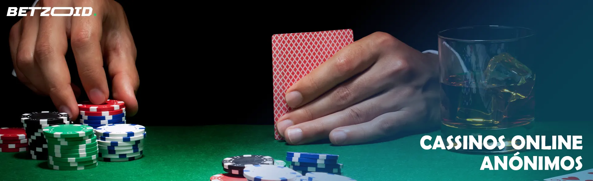 Um jogador segura cartas ao lado de fichas de cassino e uma bebida em um copo.