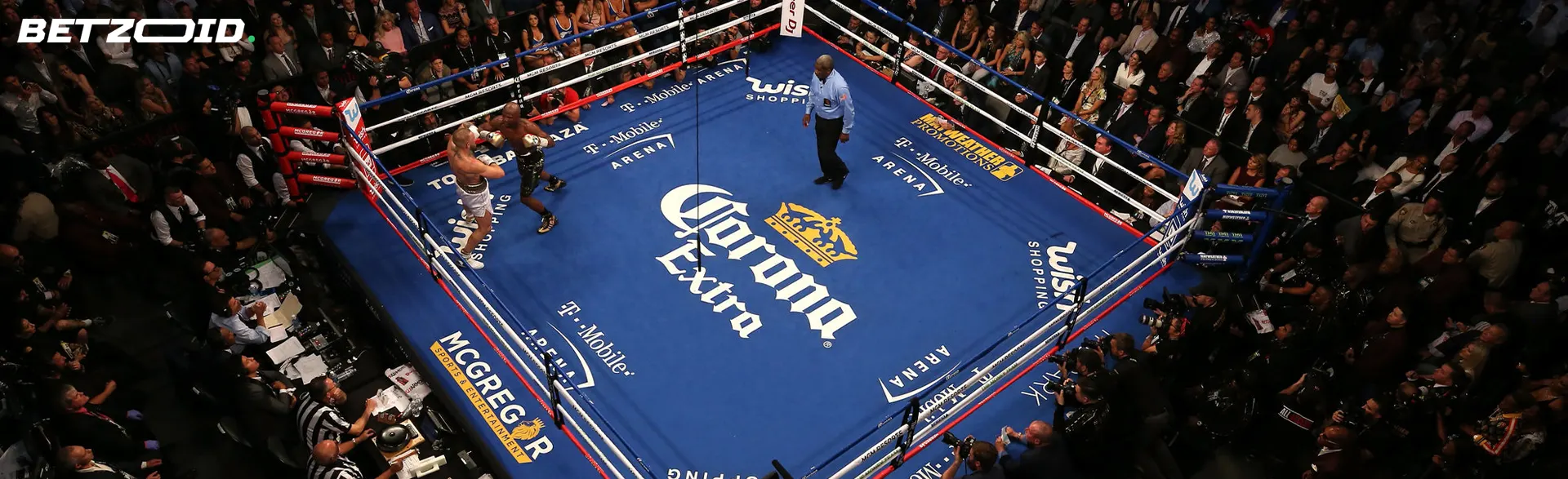 Boxers fight in the ring surrounded by spectators.