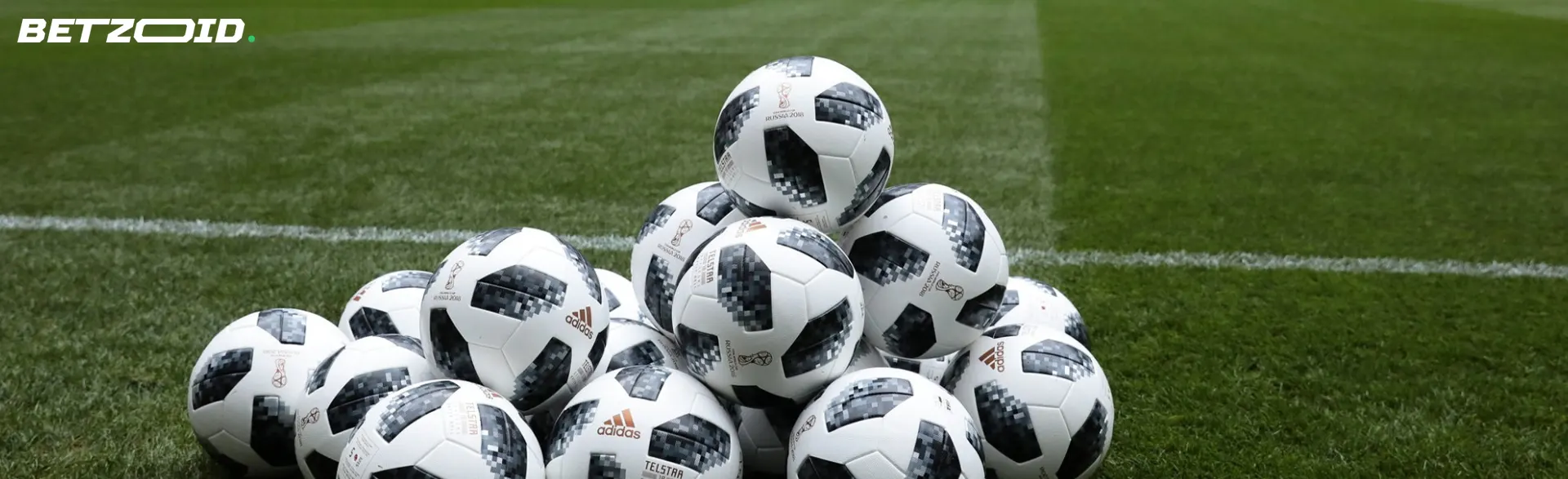 A pile of soccer balls on the grass.
