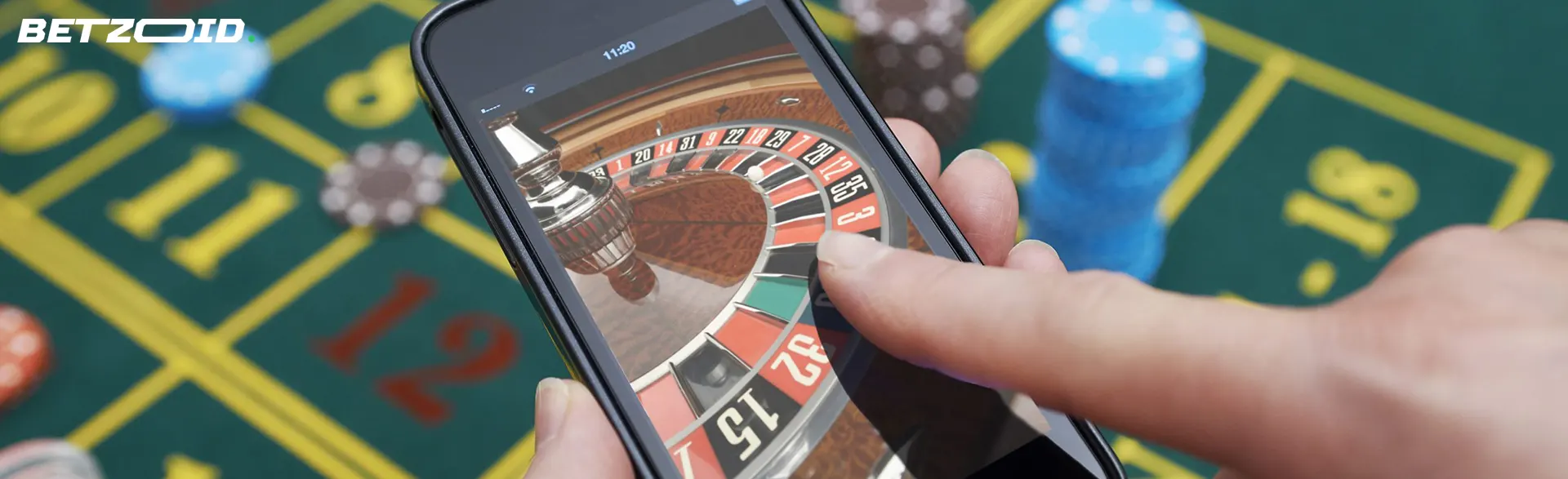 カジノのテーブルの背景にあるプレーヤーの手の中のスマートフォン。