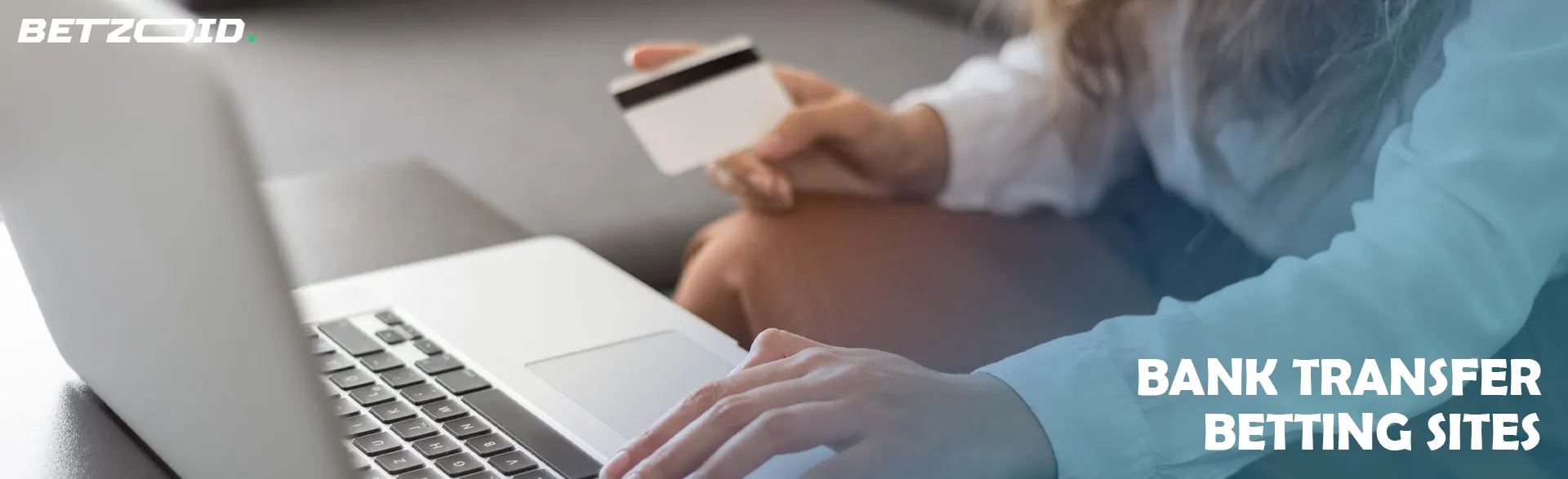Woman holding a bank card in front of a laptop.
