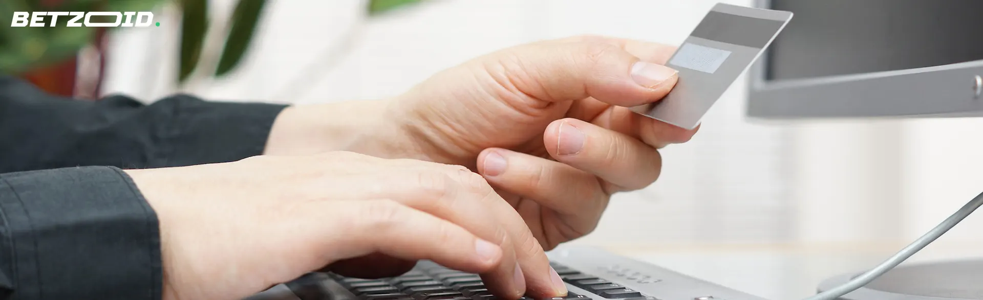 A man holds a bank card next to a laptop.