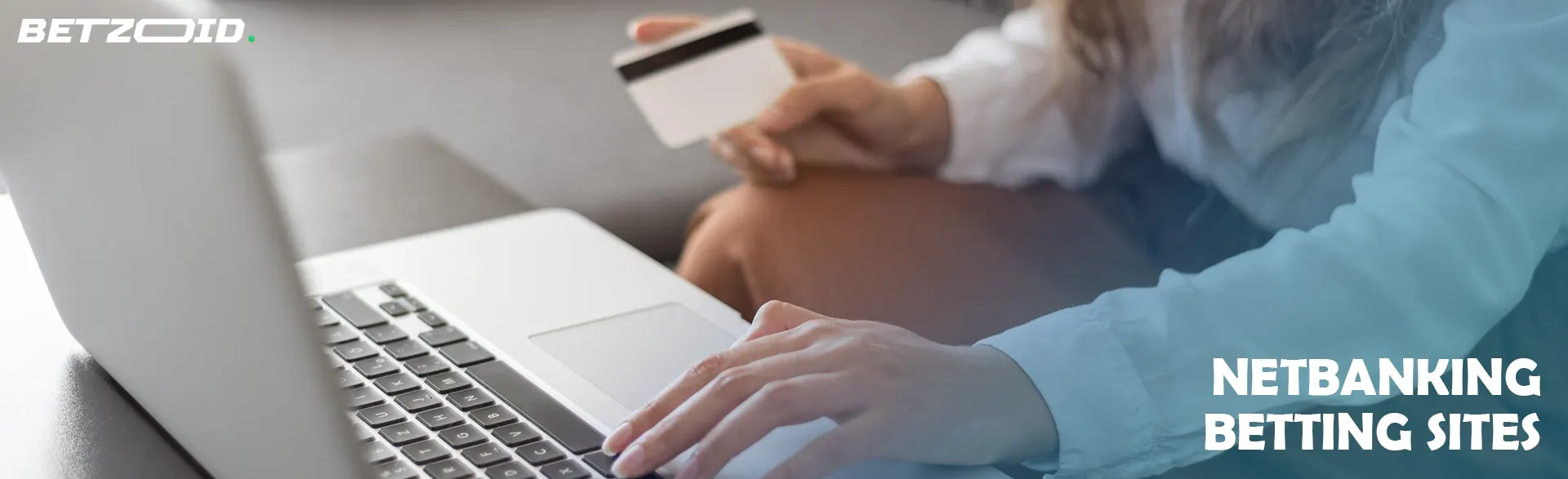 Woman holding a bank card while sitting in front of a laptop.