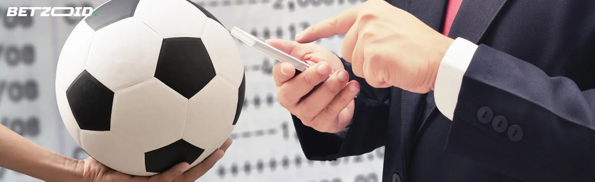 A man holds a smartphone next to a soccer ball.
