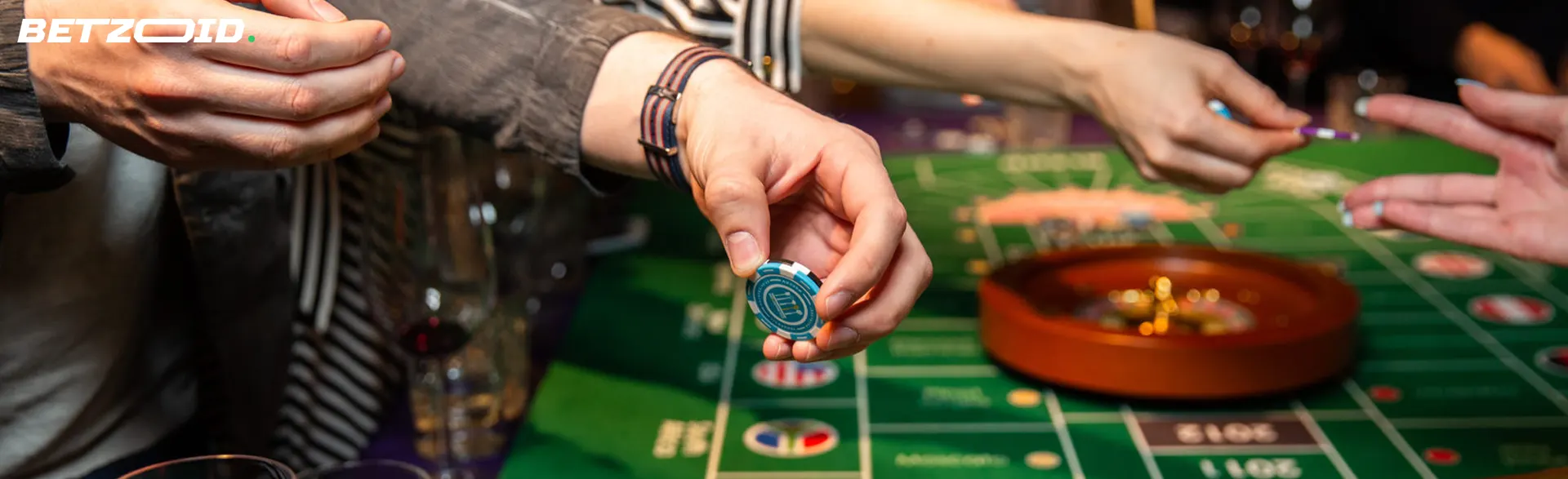 A player holds chips above a roulette table.