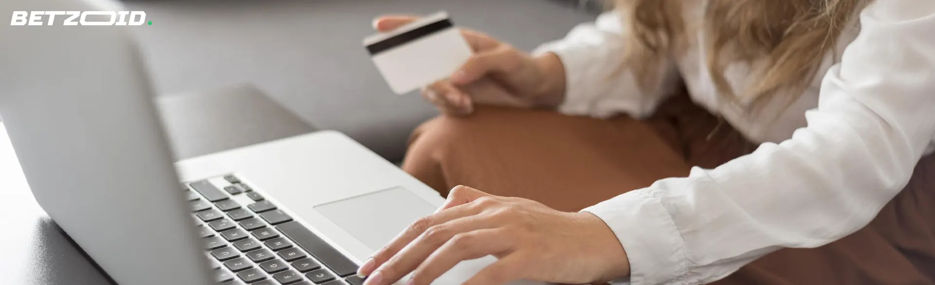 Mulher segurando um cartão bancário ao lado de um laptop.